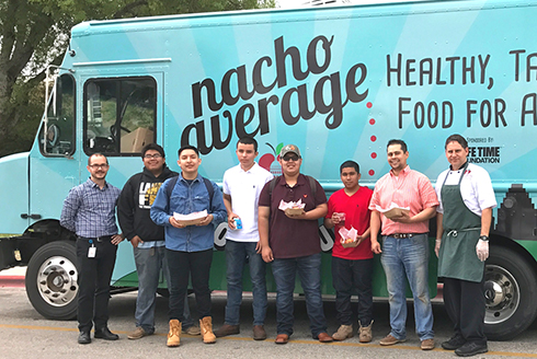 Group of highschool students standing in front of the Nacho Average food truck holding food
