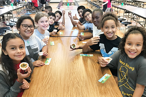 Ten elementary school students in cafeteria sampling baba ganoush