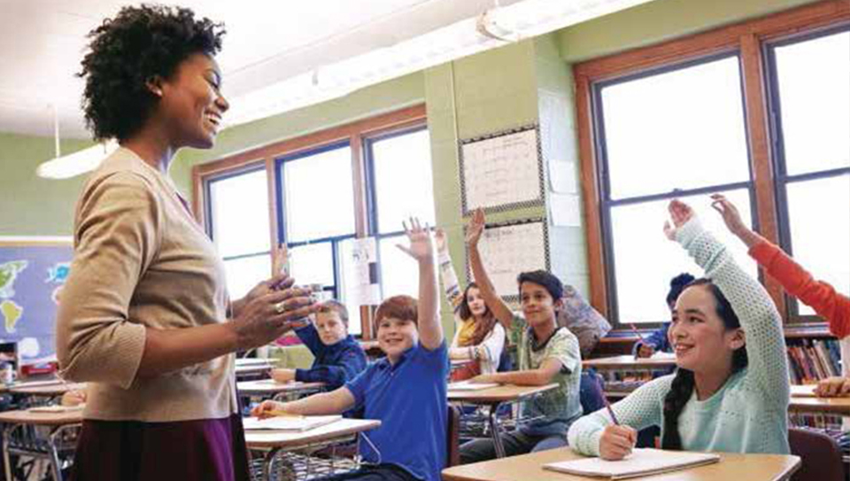 Middle school students with their hands raised as an African American female teacher smiles at them.