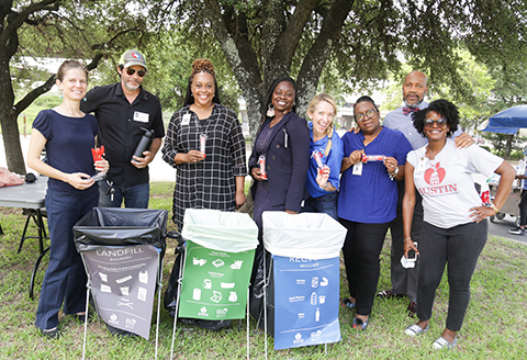 Zero-waste event coordinators standing by the Lanfill, compoast and recycling bins marked with example trash items