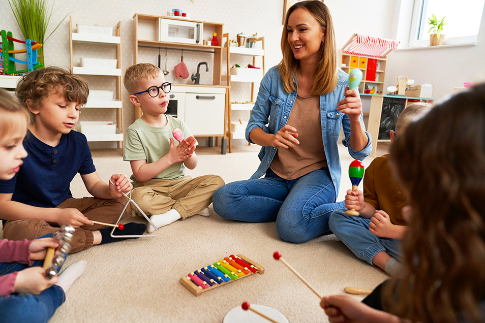 A group of students sitting on the floor playing instruments with the teacher.