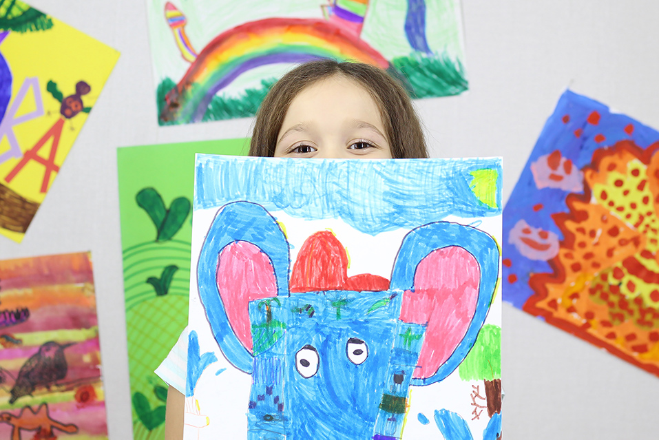 A student holding up their colorful drawing in front of their face with only eyes showing.