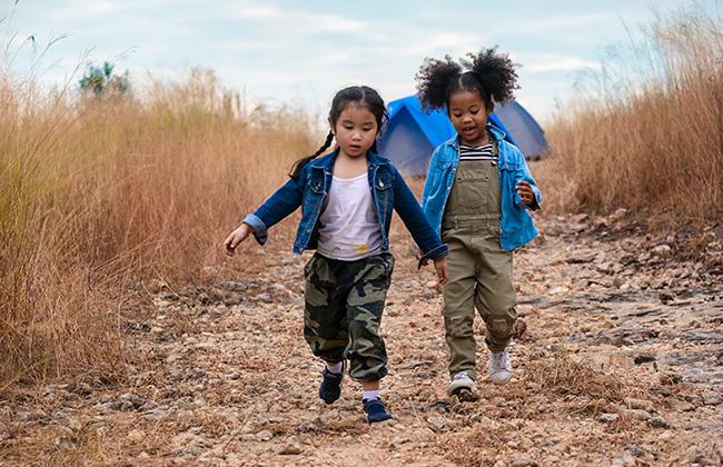 Two young African American and Asian children walking from a camp site